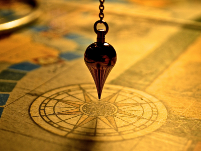 Imagem conceitual de um pêndulo apontando para o centro de uma bússola, representando a radiestesia como guia para encontrar clareza e direção.